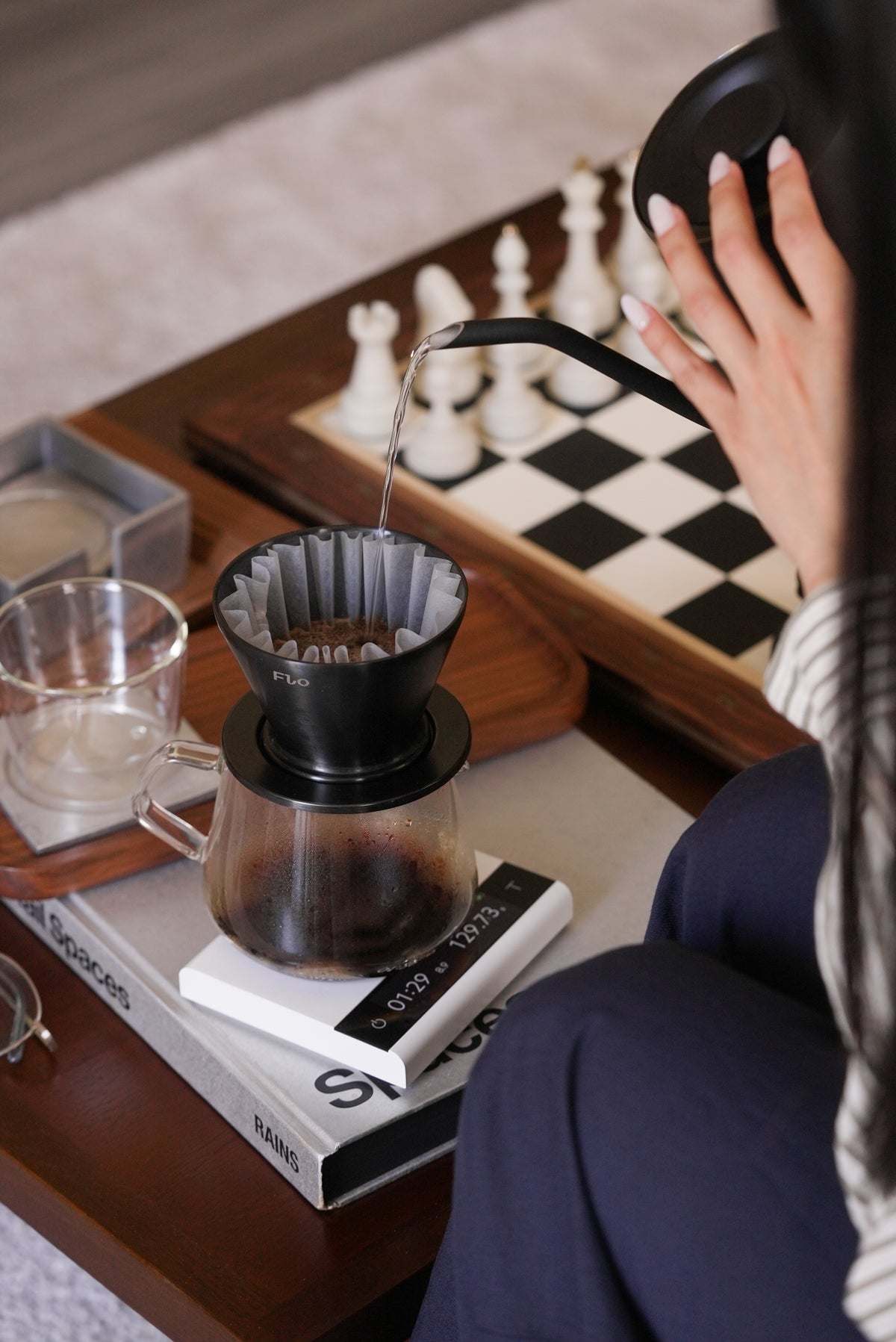 Brewing through a black FLO dripper with Varia kettle and scale beside a chessboard